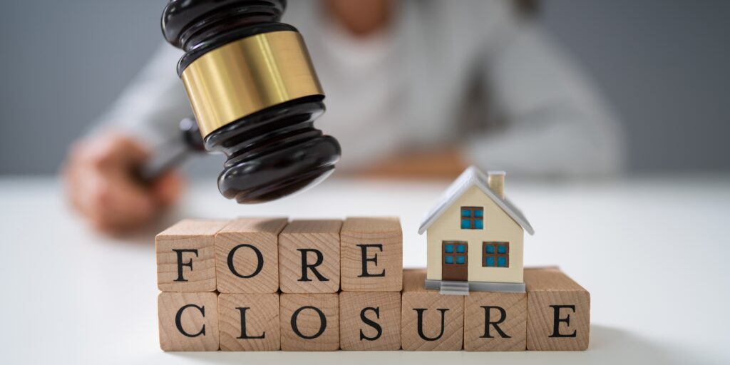 Wooden blocks spelling foreclosure with a miniature house and a legal gavel in the background representing judicial foreclosure defense in South Florida.
